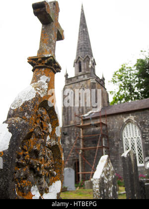 Détail d'un old weathered pierre tombale avec une église catholique rural dans l'arrière-plan dans le comté de Cork, Irlande. Banque D'Images