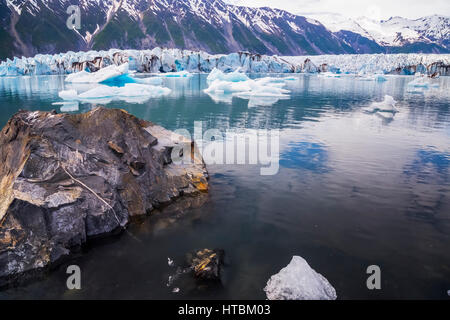 Un gros rocher se trouve dans une lagune contenant plusieurs icebergs vêlé sur la face du glacier de l'Ours (en arrière-plan) dans le Parc National de Kenai Fjords Banque D'Images