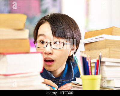 Élève asiatique à lunettes semble être choqué par les livres qu'il a à lire. Banque D'Images