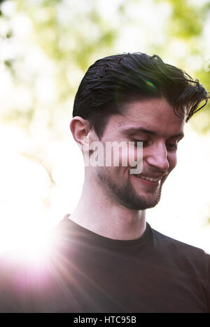 Jeune homme aux cheveux noirs et la barbe droite, hipster, portant des T-shirt noir, portrait dans le jardin. Heures de lumière d'or. Les rayons du soleil sur l'épaule Banque D'Images