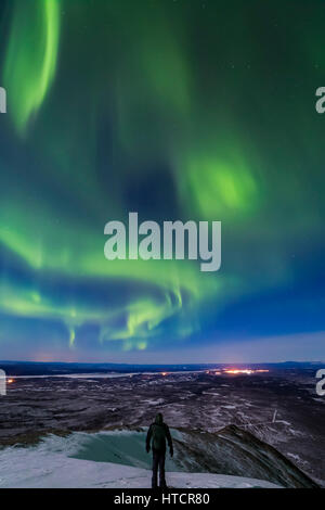 Un homme observe les aurores boréales depuis le sommet de Donnelly Dome au sud de fort Greely et Delta Junction, dont les lumières sont visibles dans T... Banque D'Images