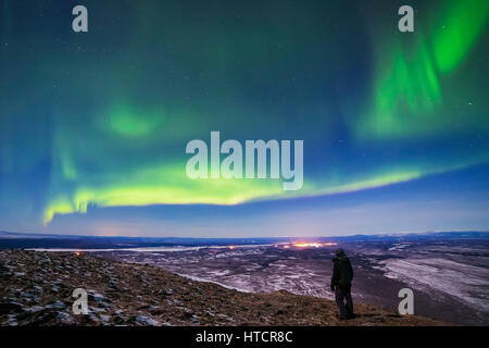 Un homme observe les aurores boréales depuis le sommet de Donnelly Dome au sud de fort Greely et Delta Junction, dont les lumières sont visibles dans T... Banque D'Images