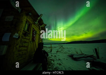 Un homme observe l'aurora de l'escalier d'une cabane de Quartz Lake State Recreation Area à l'hiver, l'intérieur de l'Alaska, USA Banque D'Images