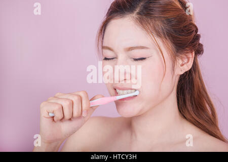 Belle femme malheureuse se brosser les dents sur fond rose Banque D'Images