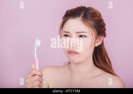 Belle femme malheureuse se brosser les dents sur fond rose Banque D'Images