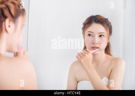 Femme en serviette de bain se brosser les dents avec miroir dans la salle de bains Banque D'Images