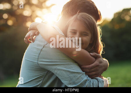 Portrait of a smiling little girl hugging affectueusement son père tout en profitant d'une journée ensemble dans un parc sous le soleil d'après-midi d'été Banque D'Images
