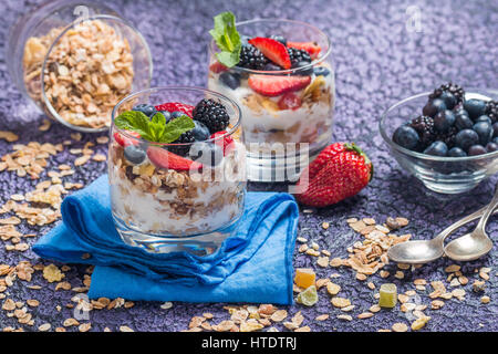 Du yaourt fait maison avec des granola et de baies dans de petits verres sur fond violet Banque D'Images