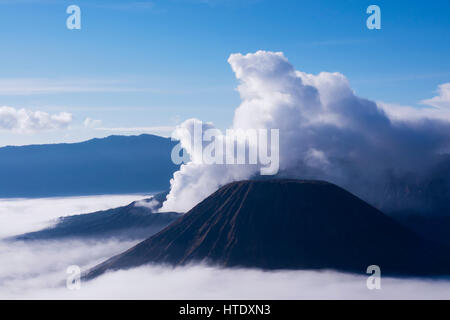 La fumée blanche qui sort des volcans entouré par des nuages blancs de brume et un ciel bleu clair vu à une distance dans l'après-midi depuis le mont Penanjakan Banque D'Images