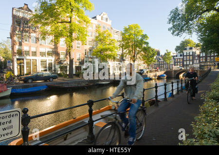 À vélo au travail le long d'un canal d'Amsterdam, chemins de remorquage sur un matin ensoleillé Banque D'Images