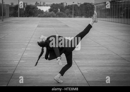 Belle jeune femme dans une veste noir et blanc danse moderne qui se déplace sur une esplanade en bois d'un quartier d'affaires moderne Banque D'Images