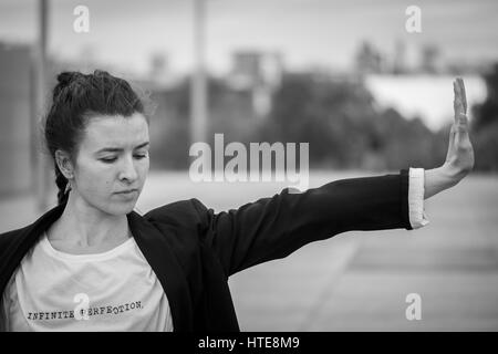 Belle jeune femme dans une veste noir et blanc danse moderne qui se déplace sur une esplanade en bois d'un quartier d'affaires moderne Banque D'Images