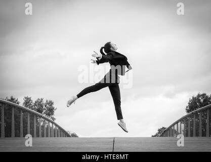 Belle jeune femme dans une veste noir et blanc danse moderne qui se déplace sur une esplanade en bois d'un quartier d'affaires moderne Banque D'Images