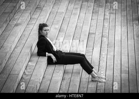 Belle jeune femme dans une veste noir et blanc danse moderne qui se déplace sur une esplanade en bois d'un quartier d'affaires moderne Banque D'Images