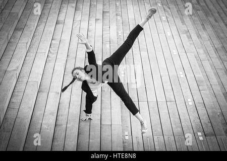 Belle jeune femme dans une veste noir et blanc danse moderne qui se déplace sur une esplanade en bois d'un quartier d'affaires moderne Banque D'Images