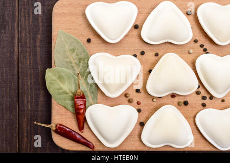 Pâte non cuite en forme de cœur (boulettes, ravioli, pelmeni), sur une planche à découper. Close up. La vue de dessus Banque D'Images