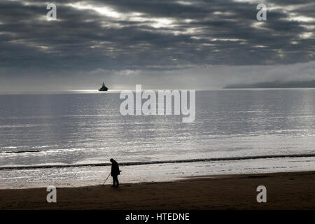 Metal detectorist sur la plage de Paignton Chasse au trésor,un bâtiment de guerre se trouve à Torbay avec Berry Head dans l'arrière-plan  Banque D'Images