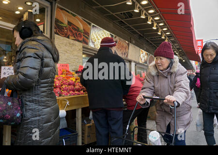 Une vieille femme chinoise poussant un chariot près d'un stand de fruits dans le quartier chinois, le rinçage, Queens, New York. Banque D'Images