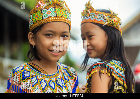 Une paire de jeunes filles en costume Dayak Kenyah sourire pour la caméra dans ce magnifique portrait de droit des enfants autochtones Banque D'Images