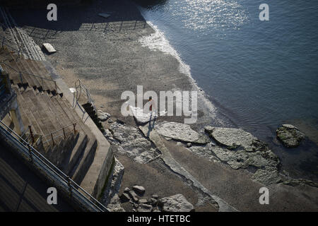 Un nageur de l'eau sort de la mer sur la plage à Plymouth Hoe par une froide journée de mars. Plymouth, Devon, Angleterre. Banque D'Images