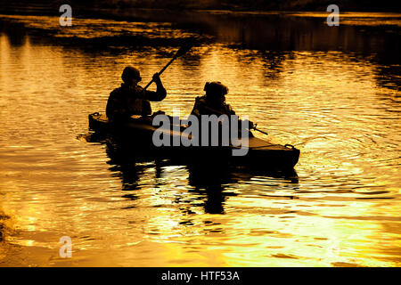 Silhouette d'hommes des forces spéciales de l'armée de pagaie en kayak. Bateau calmement de l'autre côté de la rivière, la mission de diversion, coucher de soleil Banque D'Images