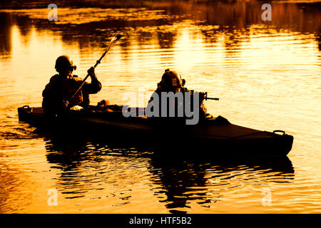 Silhouette d'hommes des forces spéciales de l'armée de pagaie en kayak. Bateau calmement de l'autre côté de la rivière, la mission de diversion, coucher de soleil Banque D'Images