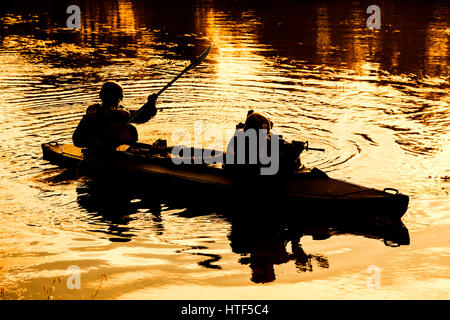 Silhouette d'hommes des forces spéciales de l'armée de pagaie en kayak. Bateau calmement de l'autre côté de la rivière, la mission de diversion, coucher de soleil Banque D'Images