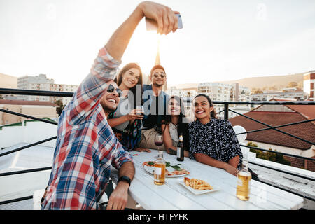 Groupe d'amis ayant une partie sur le toit en faisant un. selfies Heureux et joyeux jeunes taking self portrait au cours de soirée sur le toit. Banque D'Images