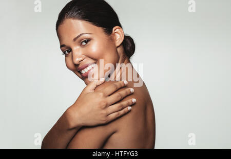 Portrait de jolie femme souriante couvrant son corps avec ses mains et à la caméra à contre fond gris. Close up of female model avec bel Banque D'Images