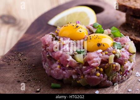 Steak tartare dans l'anneau en forme de moule, surmontée de deux jaunes d'oeuf de caille et servi avec pain de seigle sur planche à découper en bois Banque D'Images