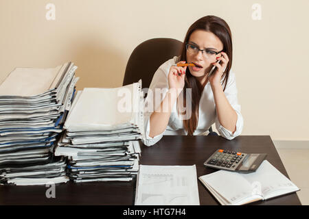 Les jeunes filles à l'aide de lunettes comptable cellulaire au travail, des piles de documents sur la table Banque D'Images