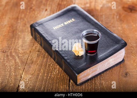 Prendre la communion. Tasse de verre avec du vin rouge, du pain et de la Sainte Bible sur table en bois close-up. Se concentrer sur le verre Banque D'Images