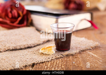 Prendre la communion. Tasse de verre avec du vin rouge, du pain et de la Sainte Bible sur table en bois close-up. L'accent sur le pain Banque D'Images