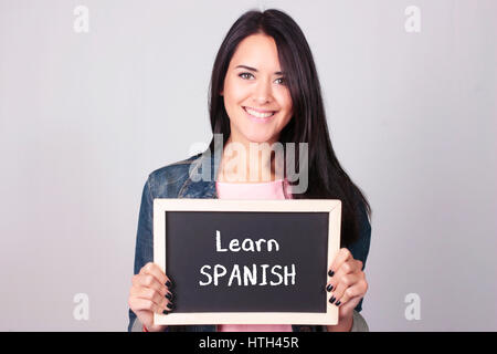 Belle Jeune femme tenant une ardoise qu'dit Apprendre l'espagnol. Banque D'Images