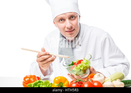 Smiling chef peremshivaet salade de légumes avec une cuillère en bois sur fond blanc Banque D'Images
