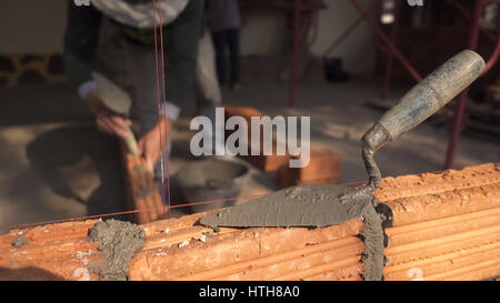 Travailleur maçon maçonnerie en brique de l'installation sur un mur extérieur avec une truelle couteau à mastic Banque D'Images
