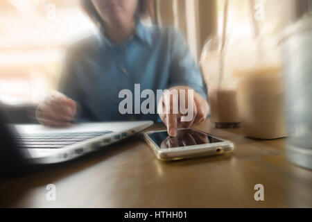 Young Asian woman hipster saisie sur écran du téléphone mobile tout en travaillant avec un ordinateur portable dans un café. Offres d'activité de démarrage d'entreprise en ligne Banque D'Images