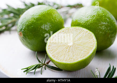 Limes et romarin frais sur une planche à découper en bois blanc Banque D'Images