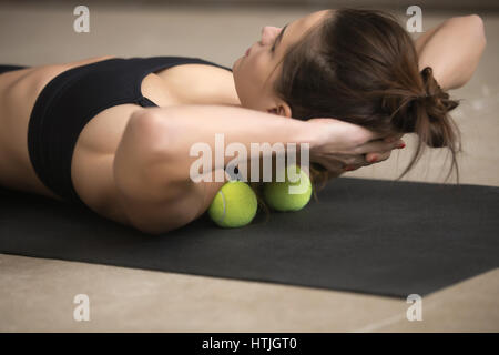 Jeune femme sportive pratiquant la technique de l'auto-massage avec tennis Banque D'Images