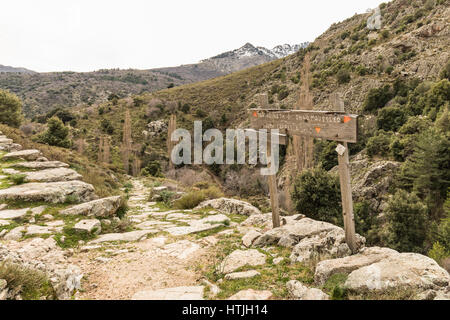 Panneau en bois sur un sentier de marche en pierre dans les collines de Balagne Corse avec des montagnes enneigées au loin Banque D'Images