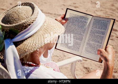 Femme adulte dans un chapeau sur une plage, la lecture d'un livre imprimé. Banque D'Images