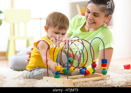 Kid garçon joue avec jouet éducatif à la maternelle à la maison. Heureux mère regardant son fils intelligent. Banque D'Images