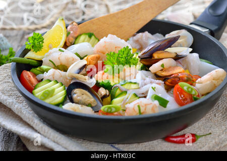 Mélange de fruits de mer frits et légumes colorés frais servi dans une poêle de fer avec des tranches de pain baguette avec du beurre aux herbes Banque D'Images