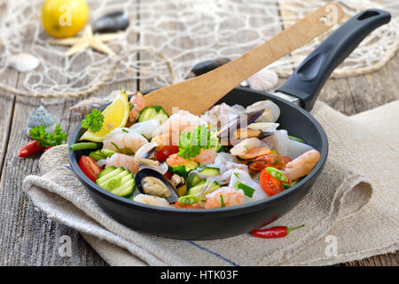 Mélange de fruits de mer frits et légumes colorés frais servi dans une poêle de fer avec des tranches de pain baguette avec du beurre aux herbes Banque D'Images