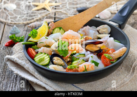 Mélange de fruits de mer frits et légumes colorés frais servi dans une poêle de fer avec des tranches de pain baguette avec du beurre aux herbes Banque D'Images