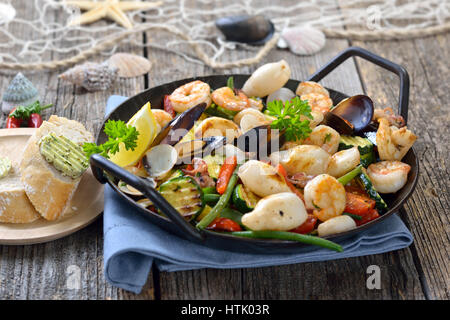 Mélange de fruits de mer frits et légumes colorés frais servi dans une poêle de fer avec des tranches de pain baguette avec du beurre aux herbes Banque D'Images