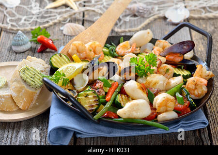 Mélange de fruits de mer frits et légumes colorés frais servi dans une poêle de fer avec des tranches de pain baguette avec du beurre aux herbes Banque D'Images