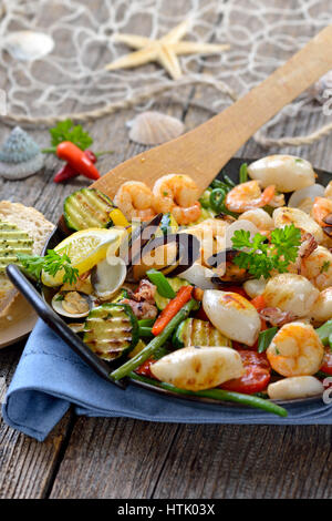 Mélange de fruits de mer frits et légumes colorés frais servi dans une poêle de fer avec des tranches de pain baguette avec du beurre aux herbes Banque D'Images