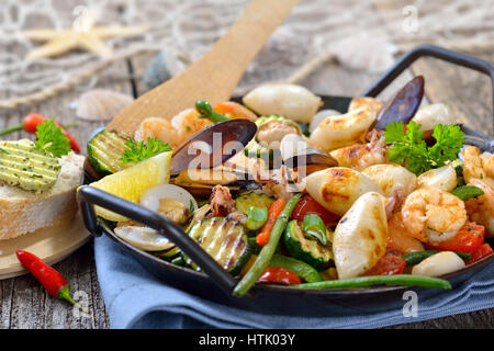 Mélange de fruits de mer frits et légumes colorés frais servi dans une poêle de fer avec des tranches de pain baguette avec du beurre aux herbes Banque D'Images