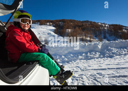 Side view portrait of smiling boy skieur assis dans le coffre contre les montagnes enneigées Banque D'Images